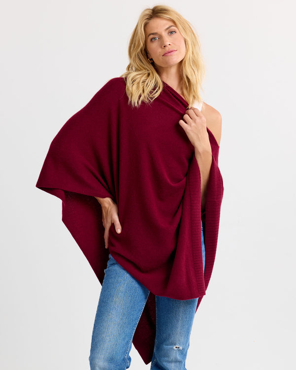 LIFESTYLE / EDITORIAL: Woman wearing a barolo-colored cashmere poncho with blue jeans against a plain background