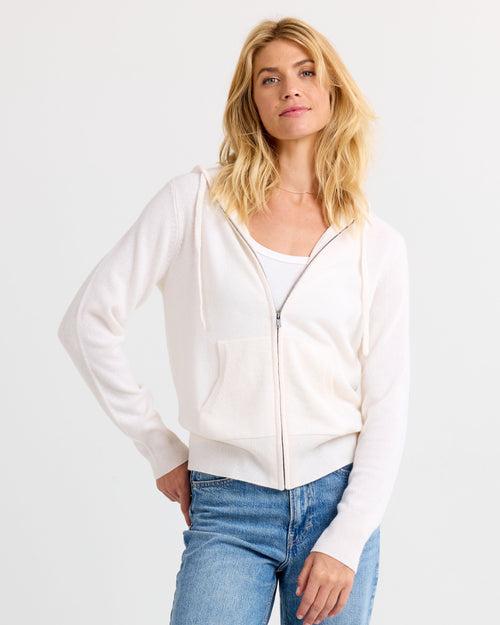 Front view image of a woman wearing an ivory zip-up cashmere hoodie and blue jeans against a white background