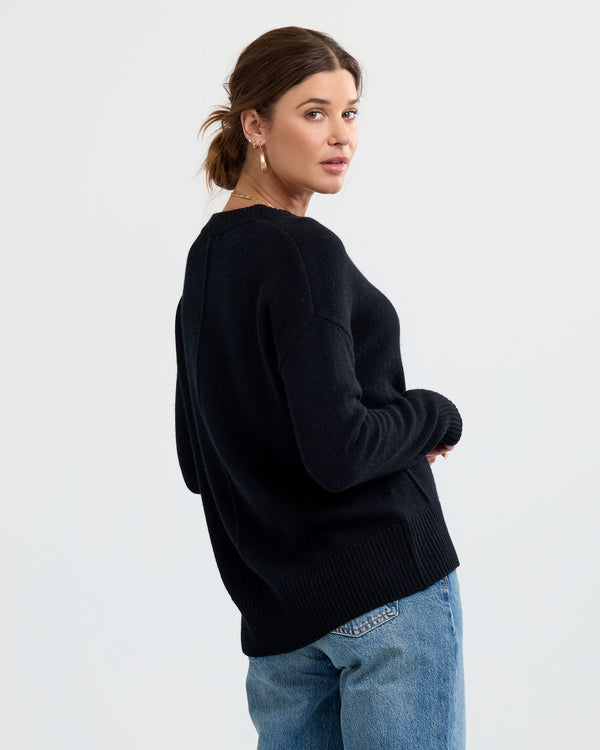 LIFESTYLE / EDITORIAL: Woman in black cashmere sweater and blue jeans, looking over shoulder against plain background