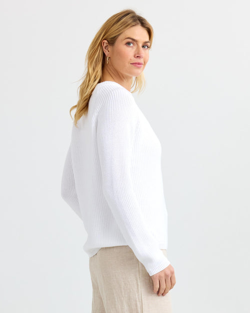 LIFESTYLE / EDITORIAL: Woman in white ribbed cashmere sweater and beige pants, side view against plain background