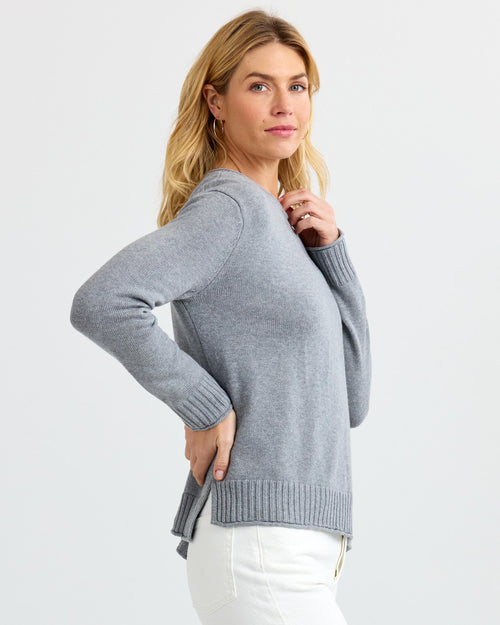 LIFESTYLE / EDITORIAL: Woman wearing light gray cashmere sweater and white pants, posing sideways against white background