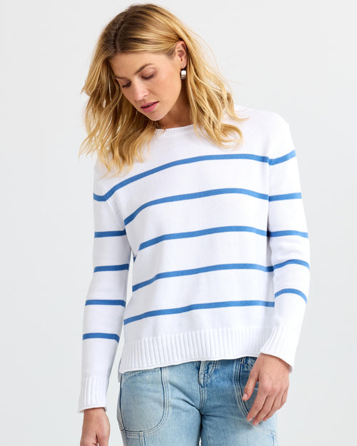 LIFESTYLE / EDITORIAL: Woman wearing white sweater with blue stripes and light blue jeans against white background