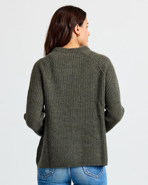 LIFESTYLE / EDITORIAL: Woman wearing dark olive ribbed cashmere sweater, back view, paired with blue jeans against white