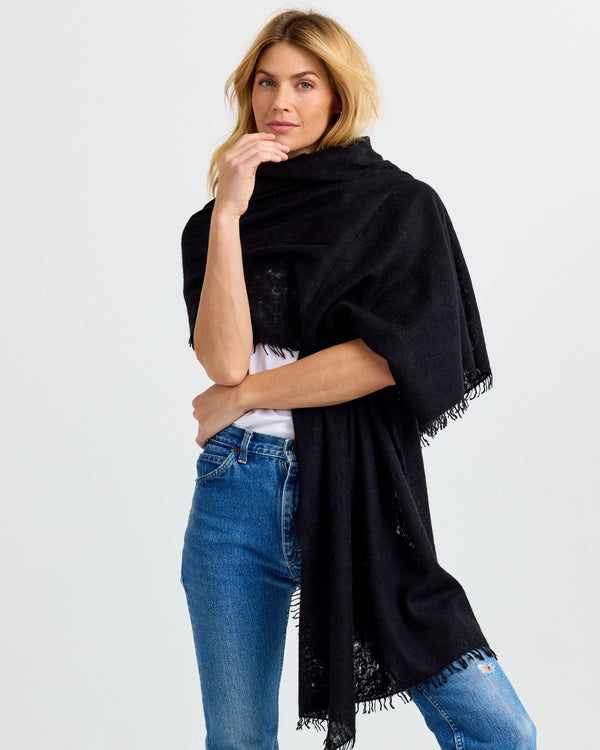 LIFESTYLE / EDITORIAL: Woman wearing black cashmere shawl over white top and blue jeans against plain background