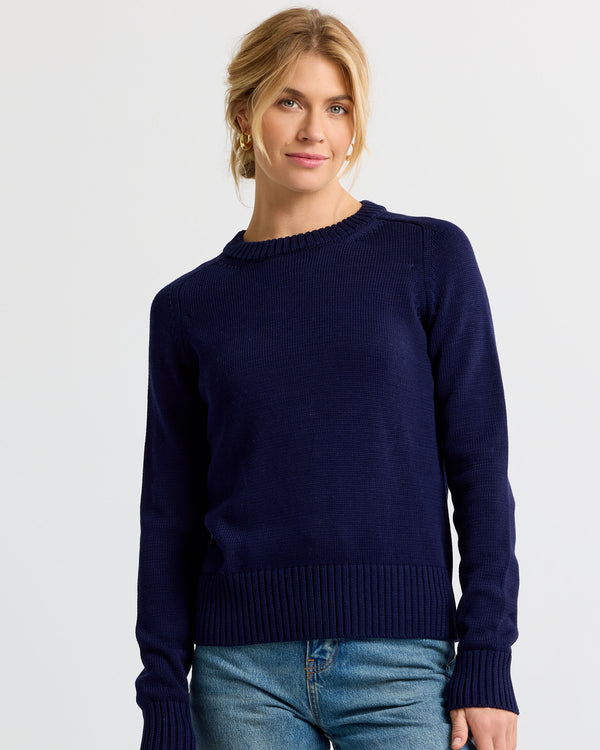 LIFESTYLE / EDITORIAL: Woman wearing navy cashmere sweater and blue jeans, standing against white background