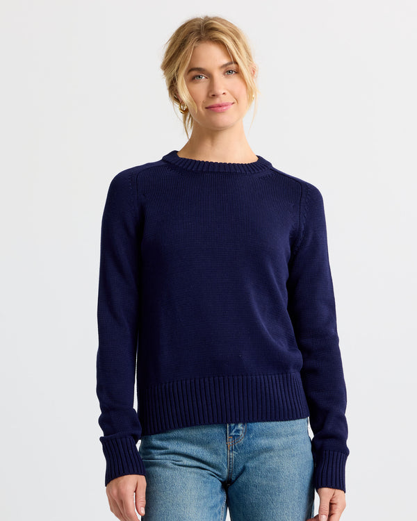 Front-facing image of a woman wearing a navy blue cashmere sweater paired with blue jeans against white background