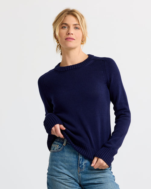 LIFESTYLE / EDITORIAL: Woman wearing navy cashmere sweater and blue jeans against plain white background