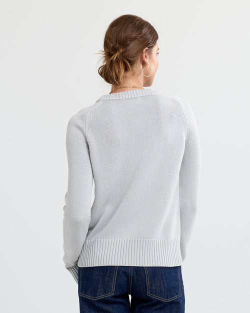 LIFESTYLE / EDITORIAL: Woman seen from back wearing light grey cashmere sweater and dark jeans against white background