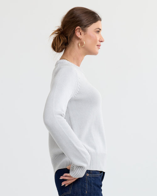 LIFESTYLE / EDITORIAL: Woman in light grey cashmere sweater and jeans, side profile against plain background