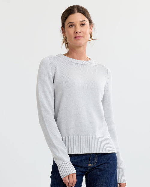 LIFESTYLE / EDITORIAL: Woman wearing light grey cashmere sweater and dark jeans against plain white background