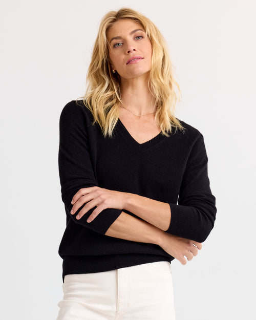 LIFESTYLE / EDITORIAL: Woman wearing black V-neck cashmere sweater and white pants, standing with arms crossed against white