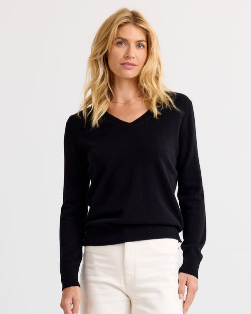 Front view image of a woman wearing a black V-neck cashmere sweater and white pants against a plain background