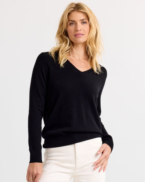 LIFESTYLE / EDITORIAL: Woman wearing black V-neck cashmere sweater and white pants against plain background