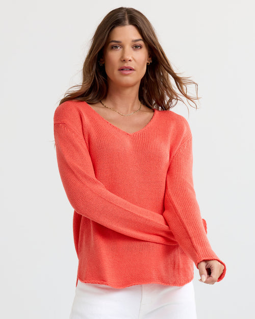 Front view image of a woman wearing coral V-neck cashmere sweater with long sleeves and white pants against white background
