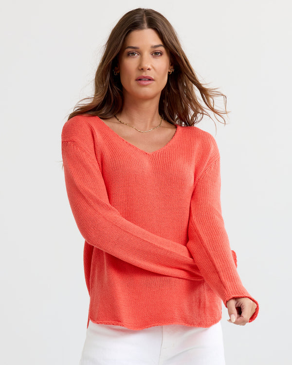 Front view image of a woman wearing coral V-neck cashmere sweater with long sleeves and white pants against white background