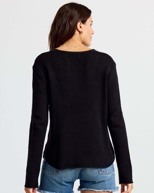 LIFESTYLE / EDITORIAL: Woman wearing black long-sleeve sweater and denim shorts, viewed from the back against white
