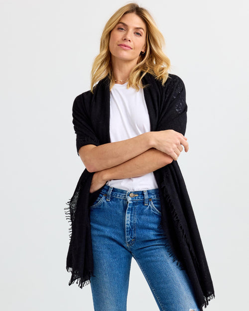 LIFESTYLE / EDITORIAL: Woman wearing black cashmere shawl over white shirt and blue jeans, standing with arms crossed