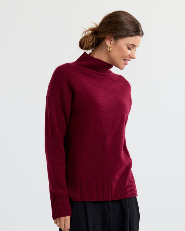 LIFESTYLE / EDITORIAL: Woman wearing a barolo red cashmere turtleneck sweater with black pants, side profile pose