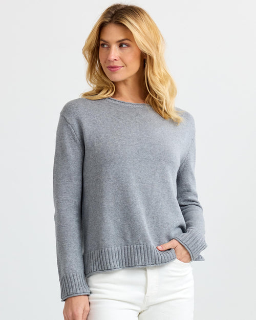 Three-quarter view image of a woman wearing a light gray cashmere sweater and white pants looking sideways
