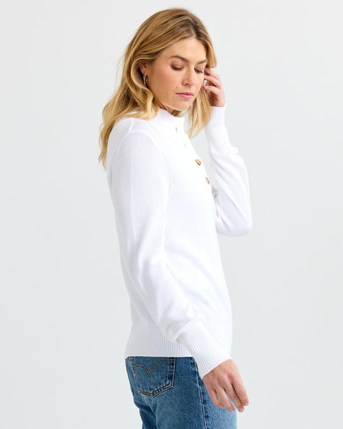 Woman in white buttoned cashmere sweater and blue jeans, side view, plain background