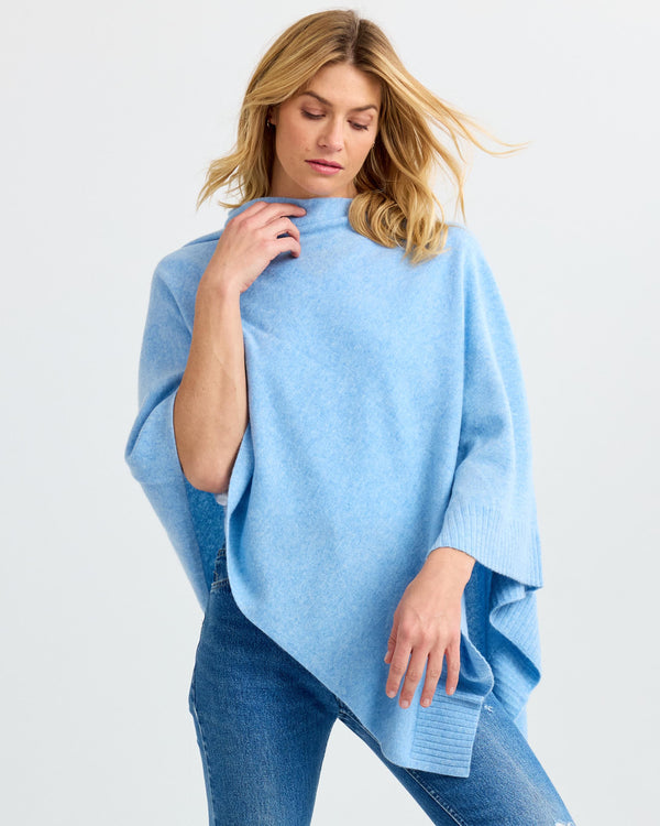 Woman wearing light blue cashmere poncho and jeans against plain background