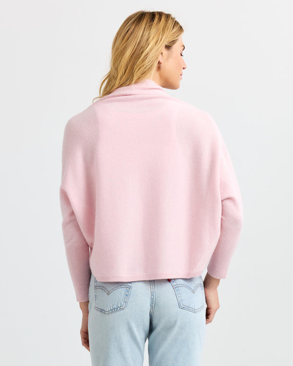 Woman wearing light pink cashmere sweater and light blue jeans, back view, studio background