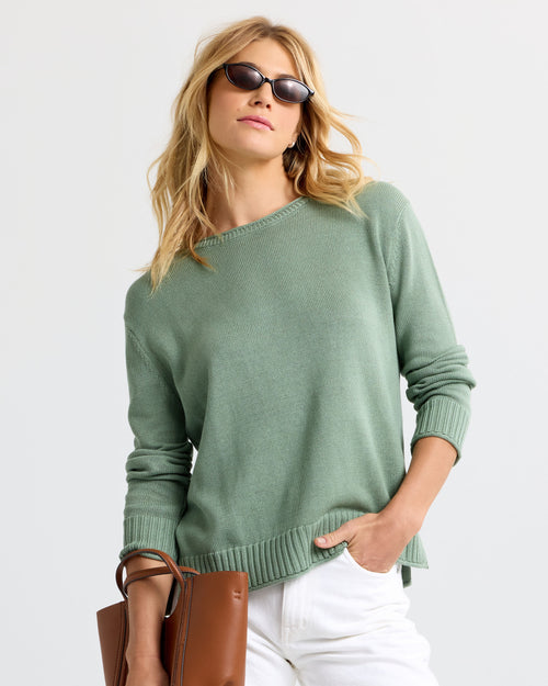 LIFESTYLE / EDITORIAL: Woman wearing sage green cashmere sweater and white pants, holding brown leather bag, sunglasses on