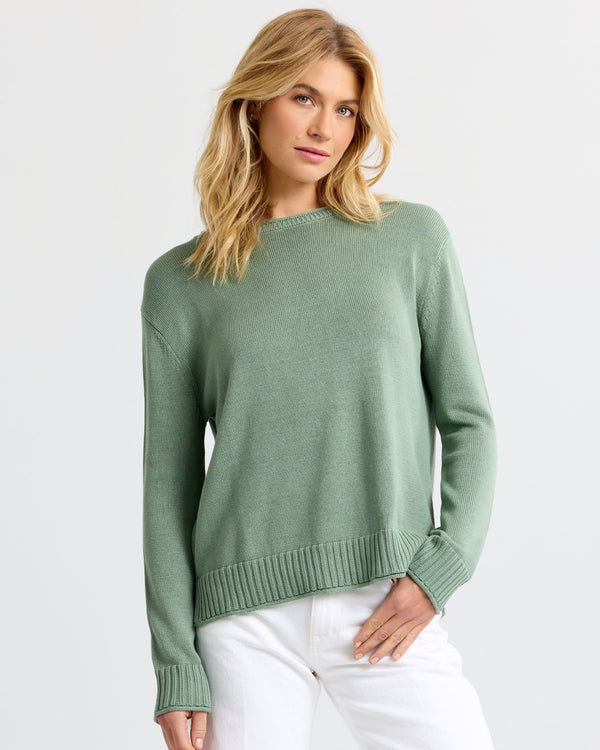 Front view image of a woman wearing a sage green cashmere sweater and white pants standing against a light background
