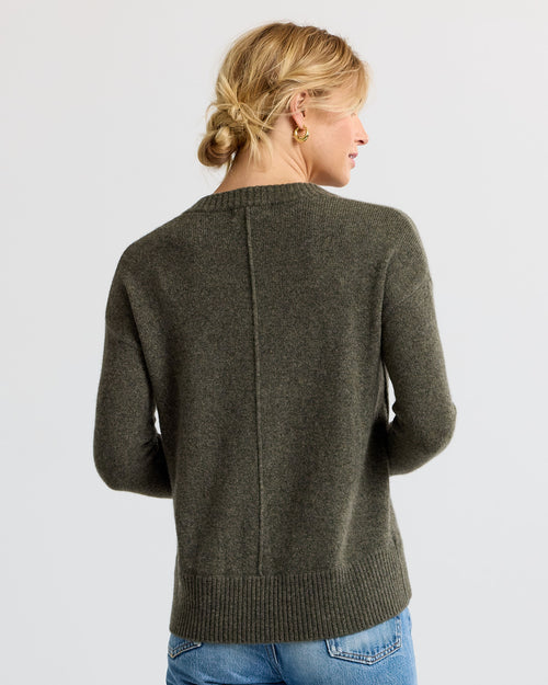 Woman wearing olive green cashmere sweater, back view, with hair in low bun and gold hoop earrings