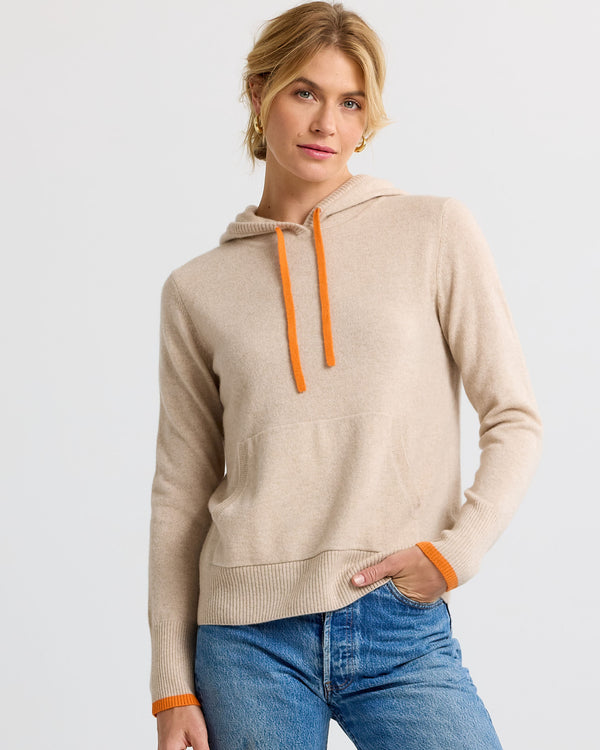 LIFESTYLE / EDITORIAL: Woman wearing beige cashmere hoodie with orange drawstrings and cuffs, paired with blue jeans