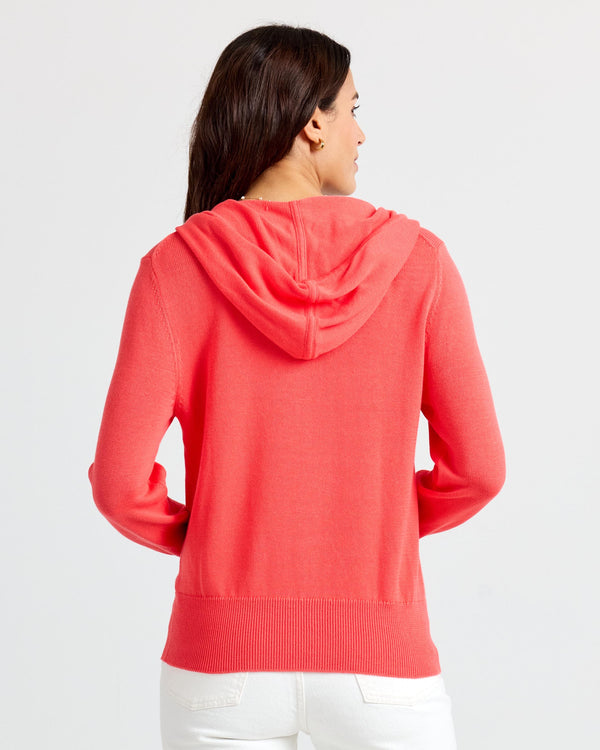 LIFESTYLE / EDITORIAL: Woman wearing coral cashmere hoodie, shown from back, with white pants against plain background