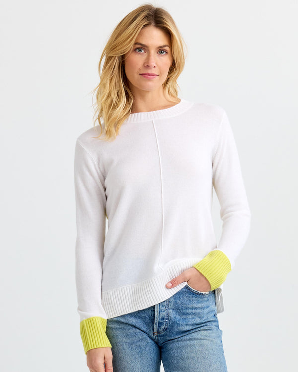 LIFESTYLE / EDITORIAL: Woman wearing white cashmere sweater with citron cuffs and blue jeans against white background