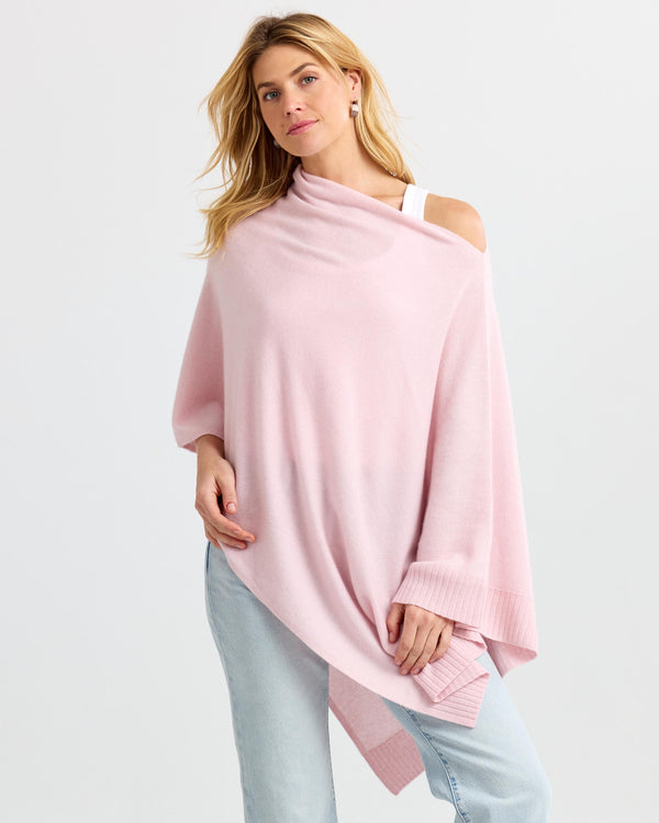 LIFESTYLE / EDITORIAL: Woman wearing blush pink cashmere poncho over white top and light blue jeans against white background