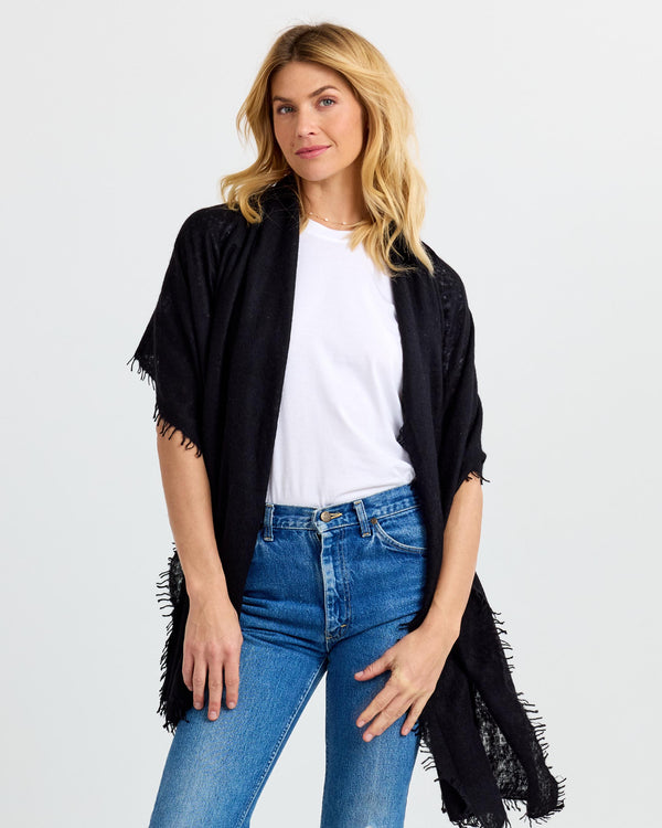 LIFESTYLE / EDITORIAL: Woman wearing black cashmere shawl over white tee and blue jeans against plain background