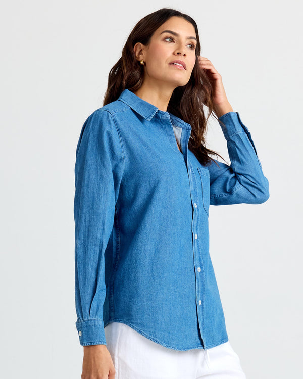 LIFESTYLE / EDITORIAL: Woman wearing medium wash denim shirt with white pants, posing against plain background
