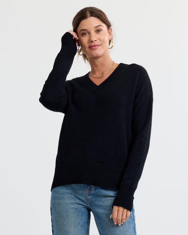 LIFESTYLE / EDITORIAL: Woman wearing black V-neck cashmere sweater and blue jeans against a plain white background