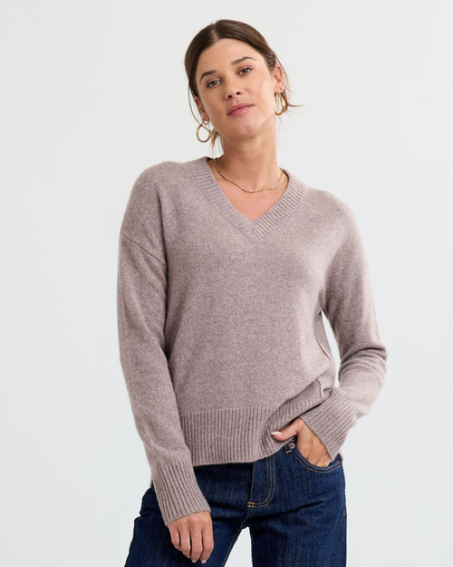 Woman wearing latte-colored V-neck cashmere sweater and jeans against plain light background