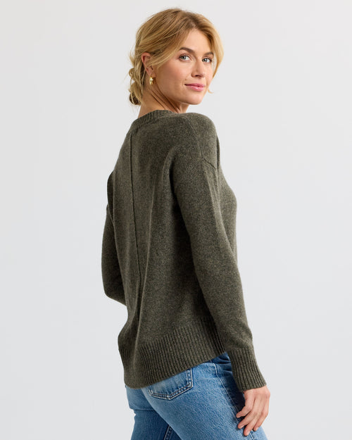 LIFESTYLE / EDITORIAL: Woman wearing olive green cashmere sweater and blue jeans, looking over shoulder against white
