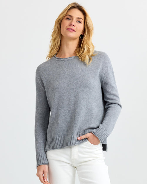 LIFESTYLE / EDITORIAL: Woman wearing grey cashmere sweater and white pants against plain white background