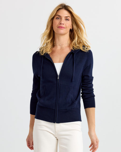 Front view image of a woman wearing a navy cashmere zip-up hoodie with white pants against a plain background