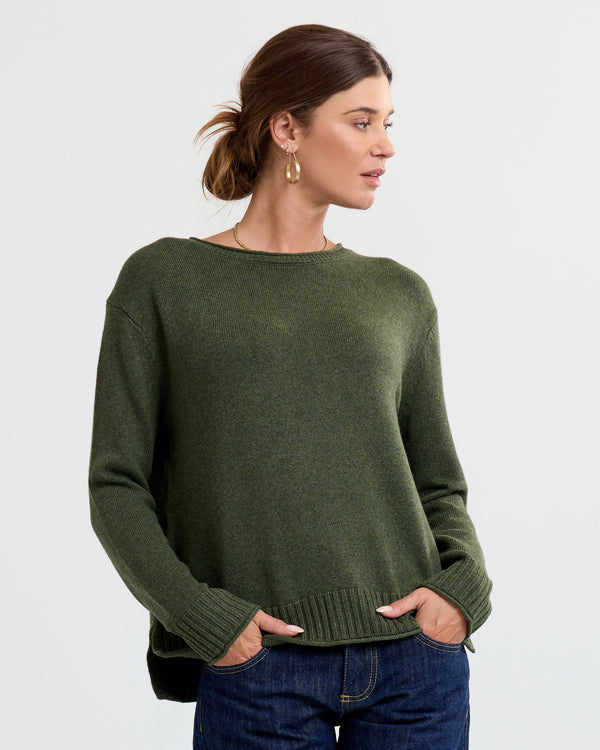 LIFESTYLE / EDITORIAL: Woman wearing olive green cashmere sweater and jeans, standing against plain background