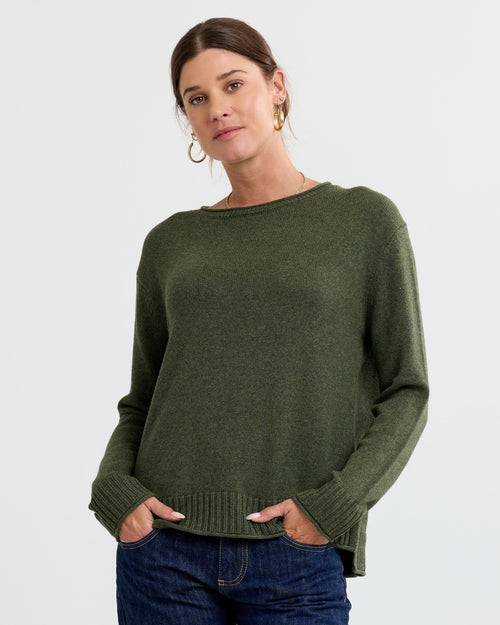 LIFESTYLE / EDITORIAL: Woman wearing olive green cashmere sweater and jeans against plain background