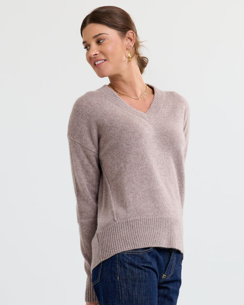 LIFESTYLE / EDITORIAL: Woman wearing latte-colored V-neck cashmere sweater and dark jeans, smiling and looking sideways