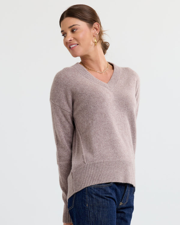 LIFESTYLE / EDITORIAL: Woman wearing latte-colored V-neck cashmere sweater and dark jeans, smiling and looking sideways
