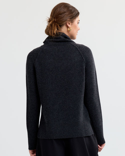 Woman wearing charcoal cashmere sweater with high neck, shown from back against plain light background