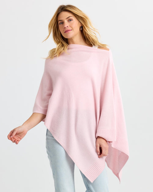 LIFESTYLE / EDITORIAL: Woman wearing blush pink asymmetrical cashmere poncho with light jeans against white background