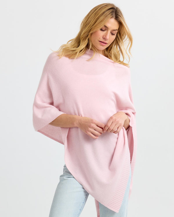 LIFESTYLE / EDITORIAL: Woman wearing blush pink cashmere poncho with light wash jeans against white background