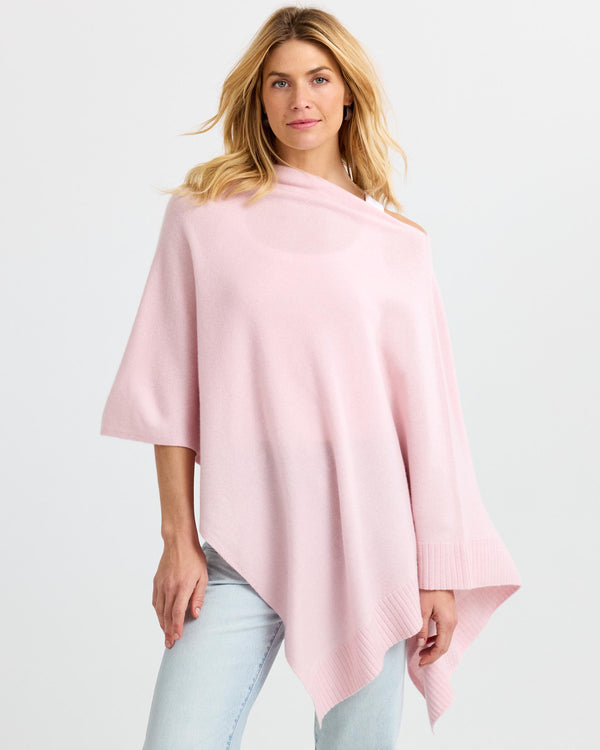 LIFESTYLE / EDITORIAL: Woman wearing blush pink cashmere poncho with asymmetrical hem and light wash jeans against white
