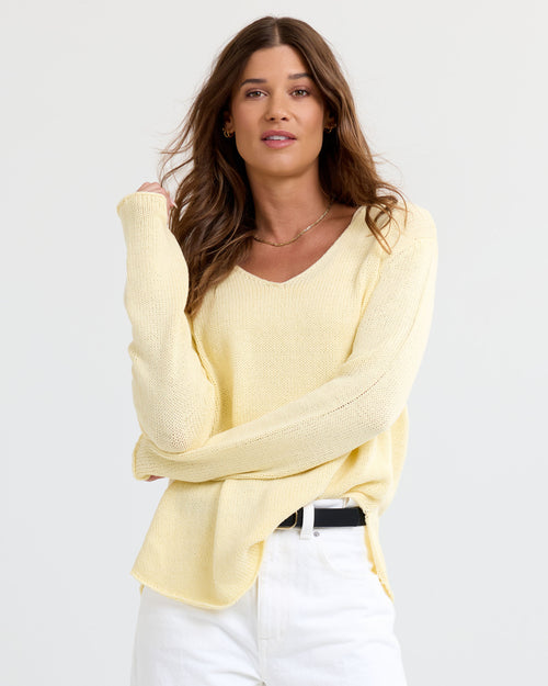 Three-quarter image of a woman wearing a buttermilk yellow V-neck cashmere sweater and white pants, arms crossed.