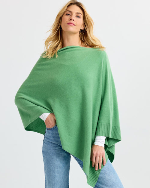 LIFESTYLE / EDITORIAL: Woman wearing a green cashmere poncho over white long sleeves and blue jeans against white background